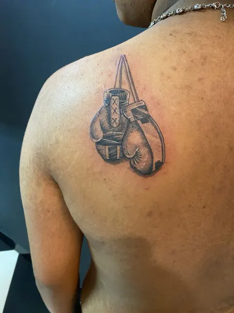 Hanging boxing gloves tattoo on the shoulder blade, by Chad Solomon