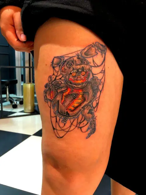 Orange demon mask in a spider web, colour thigh tattoo, by Chad Solomon