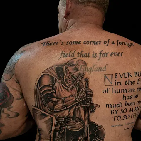 Knight kneeling with a sword beside wartime poetry lettering tattoo on the full back, by Chad Solomon
