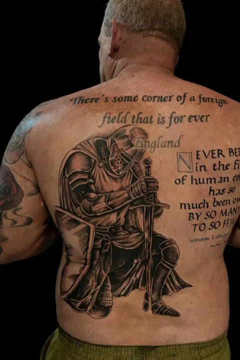 Knight kneeling with a sword beside wartime poetry lettering tattoo on the full back, by Chad Solomon
