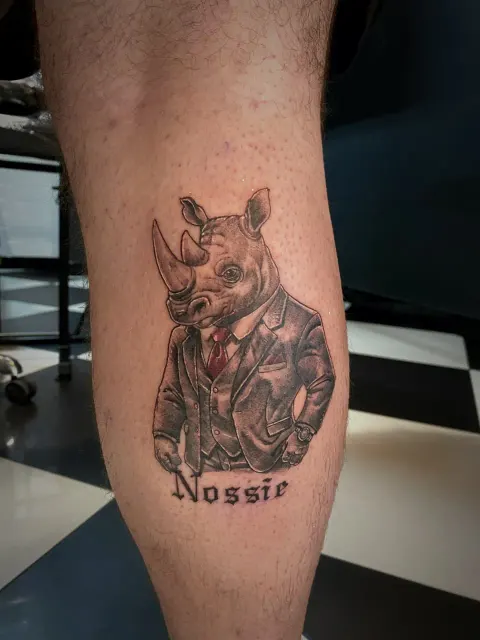 Rhino in a suit and tie tattoo on the calf, by Chad Solomon