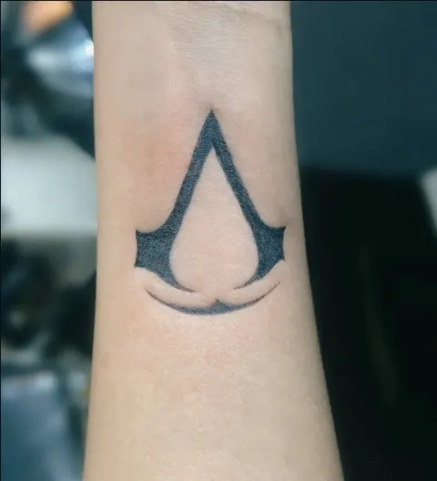Assassin’s Creed emblem tattoo on the forearm, by Kayla Grimwood