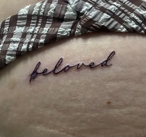 Beloved in script tattoo on the hip, by Kayla Grimwood