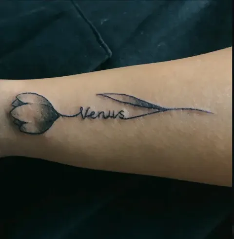 Tulip with a name in script tattoo on the forearm, by Kayla Grimwood