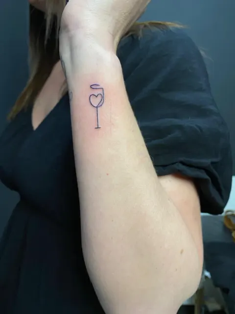 Wine glass with a heart tattoo on the forearm, by Kayla Grimwood