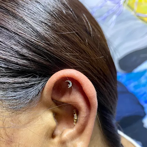 Crescent moon flat piercing with a gold conch stud, by Kelsey Messiah