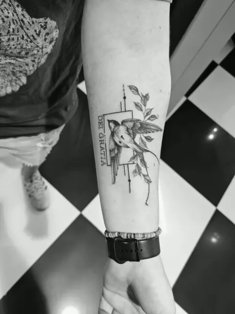 Bird with Dei Gratia lettering tattoo on the forearm, by Rob Turner