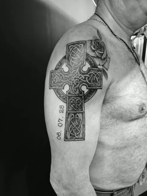 Celtic cross with a rose and memorial date tattoo on the upper arm, by Rob Turner