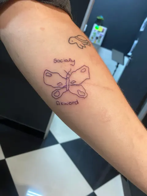 Butterfly with Socially Awkward lettering and a turtle tattoo on the forearm, by Tayla Symons