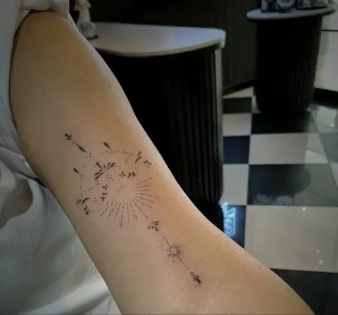 Fine line dotwork sun and arrow on the upper arm, by Tayla Symons
