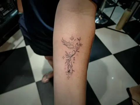 Floral stem with a bird tattoo on the calf, by Tayla Symons