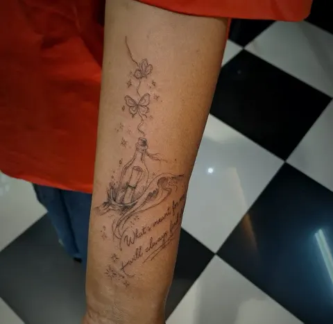 Message in a bottle with bows and script on the forearm, by Tayla Symons