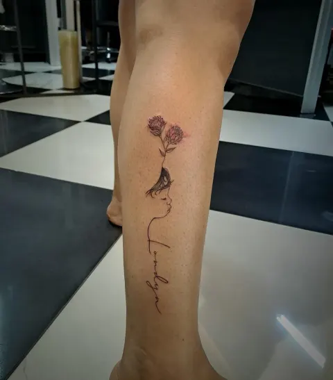 Rose and face line art with script tattoo on the calf, by Tayla Symons
